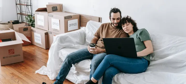 Stressed couple surrounded by boxes looking at a laptop searching for last minute removals in London